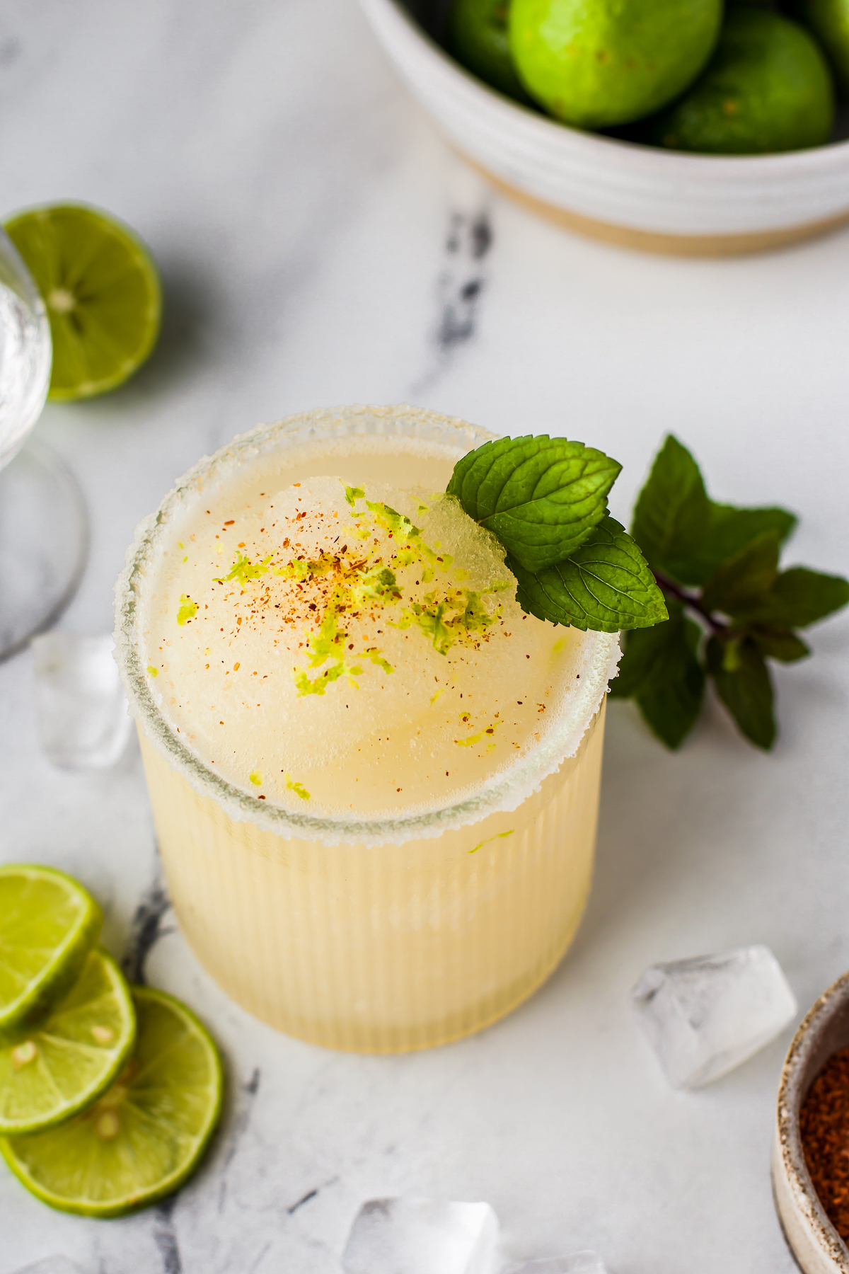 a frozen margarita in a glass with mint and chili spice garnish