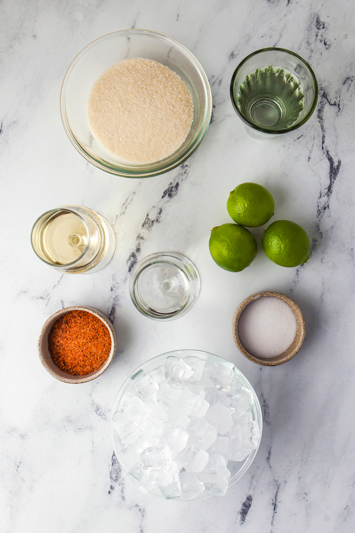 Ingredients to make margaritas on a countertop like sugar, ice, limes, mint, liquor, and salt