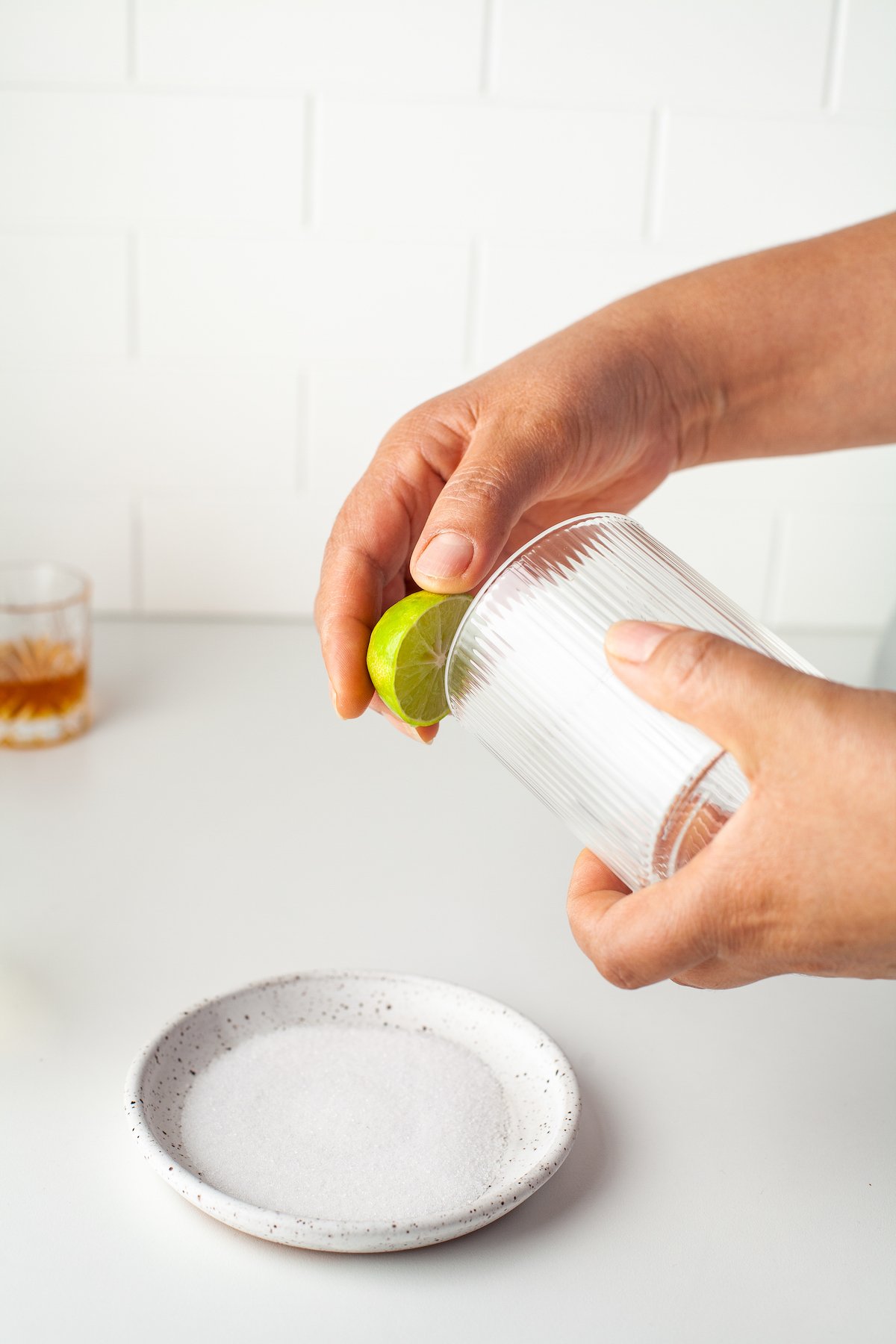 someone using a lime to coat the rim of a glass prior to dipping it into salt