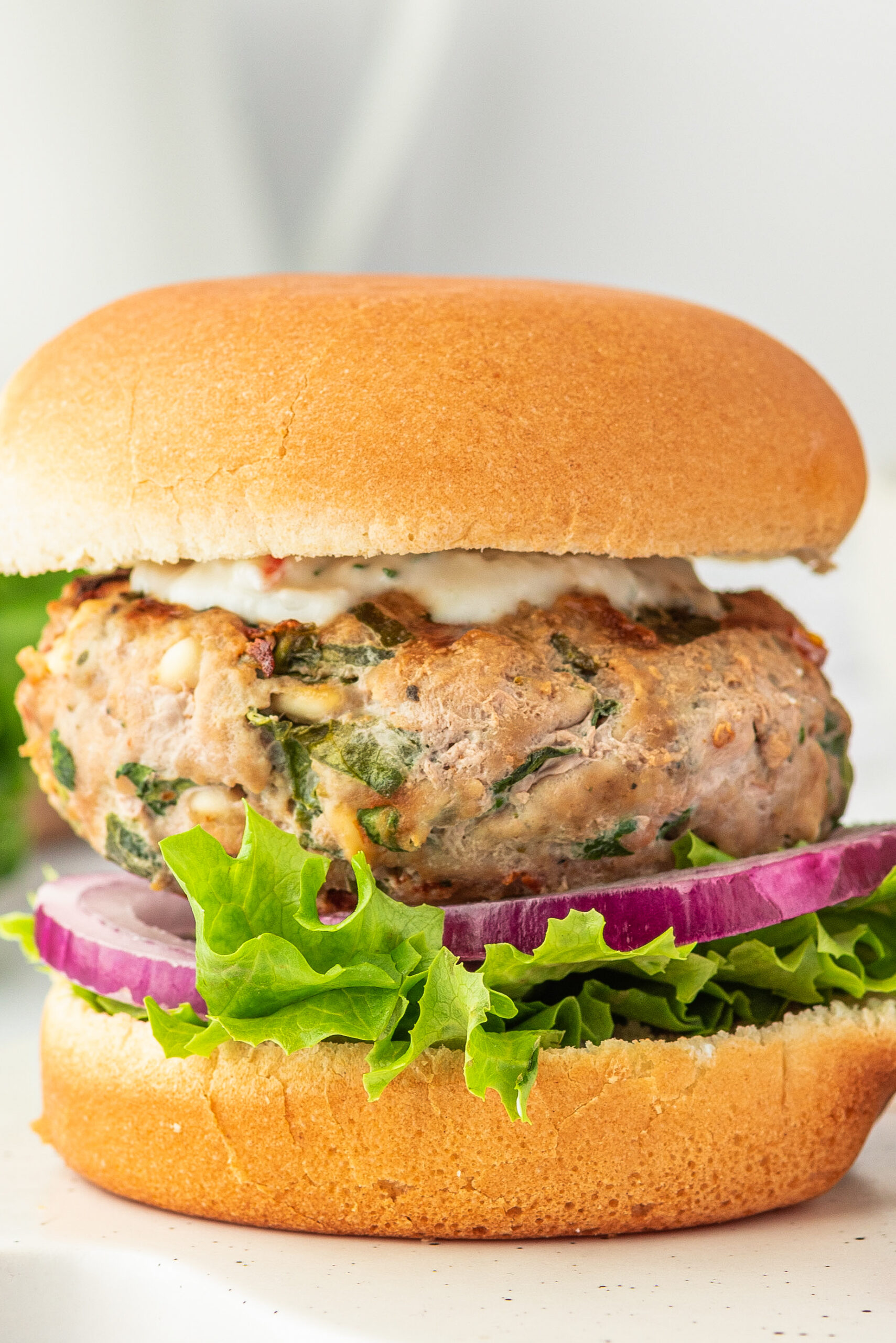 Up close image of a turkey burger with feta and spinach on a bun with tzatziki sauce.