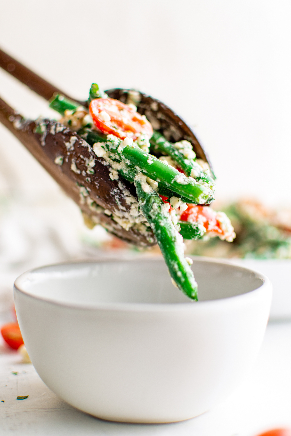 two salad tongs plating green bean salad into a white bowl