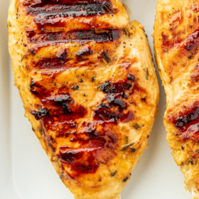 Up close image of grilled chicken in a tray with rosemary.
