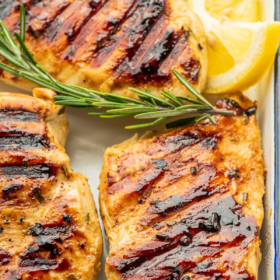 Grilled marinated chicken in a white tray with lemon wedges.