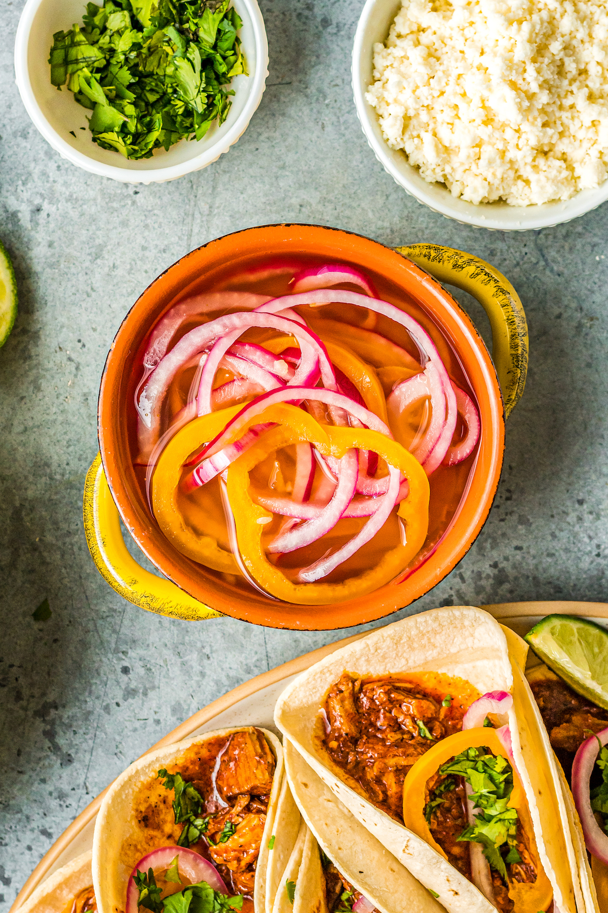 a small crock filled with pickled red onions and habaneros along side a plate of tacos