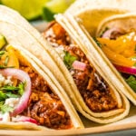 Corn tortilla tacos filled with pork, red onions, and herbs