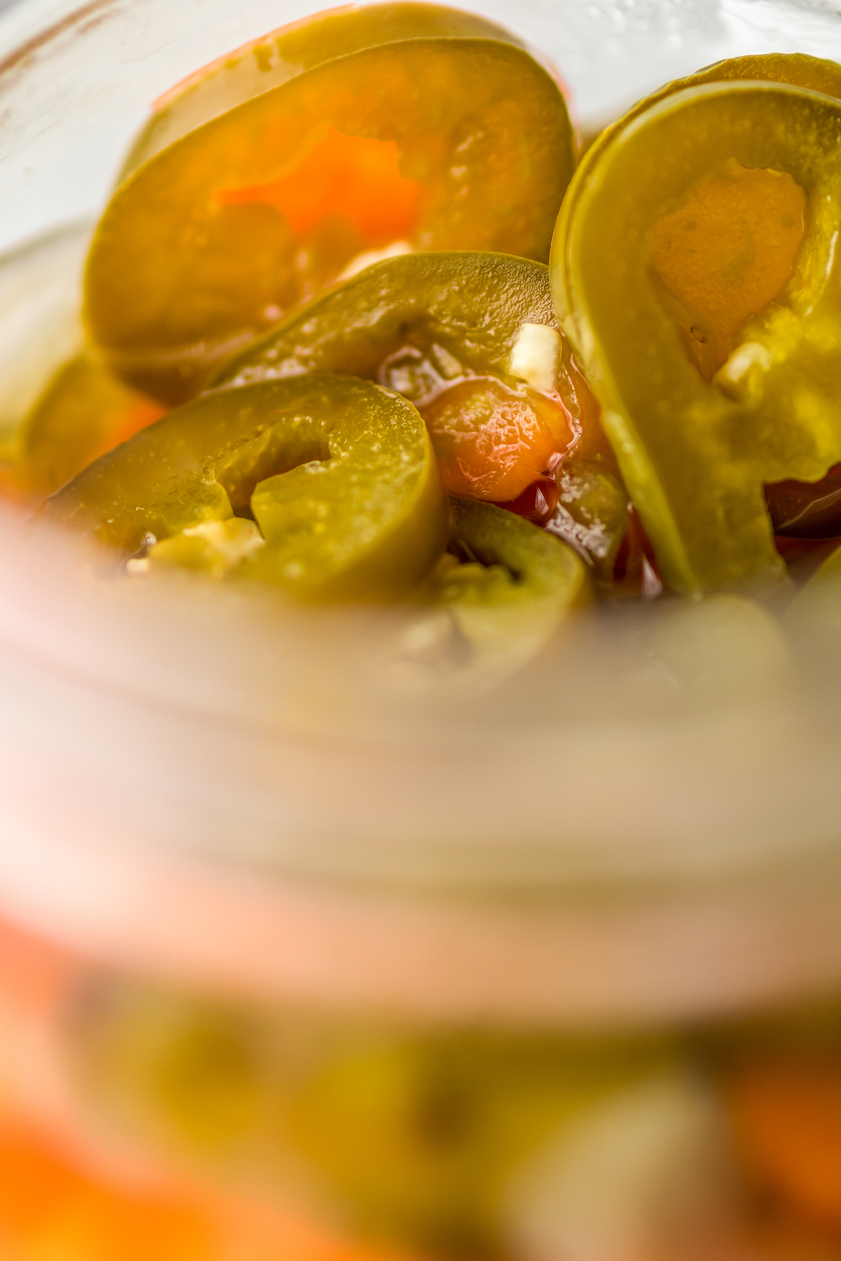 Close-up shot of sliced pickled chilis and carrots in a glass jar.