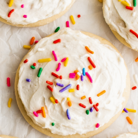 Lofthouse cookies with vanilla frosting and rainbow sprinkles arranged on parchment paper.