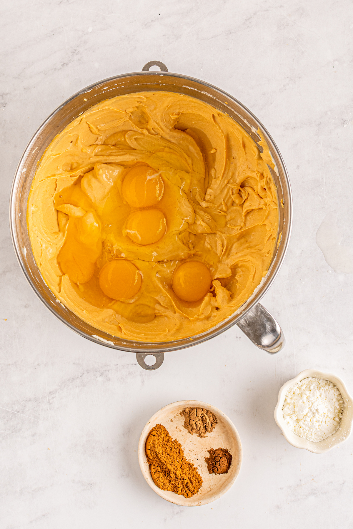 lookinginto a mixing bowl with orange cheesecake filling and cracked eggs being prepared