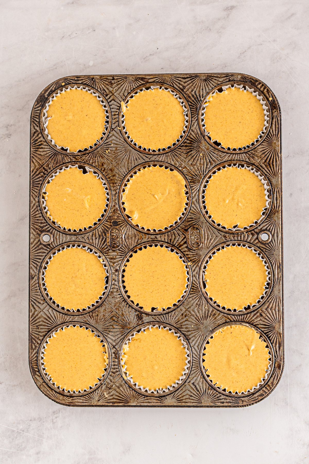 a cupcake tray filled with orange cheesecake filling