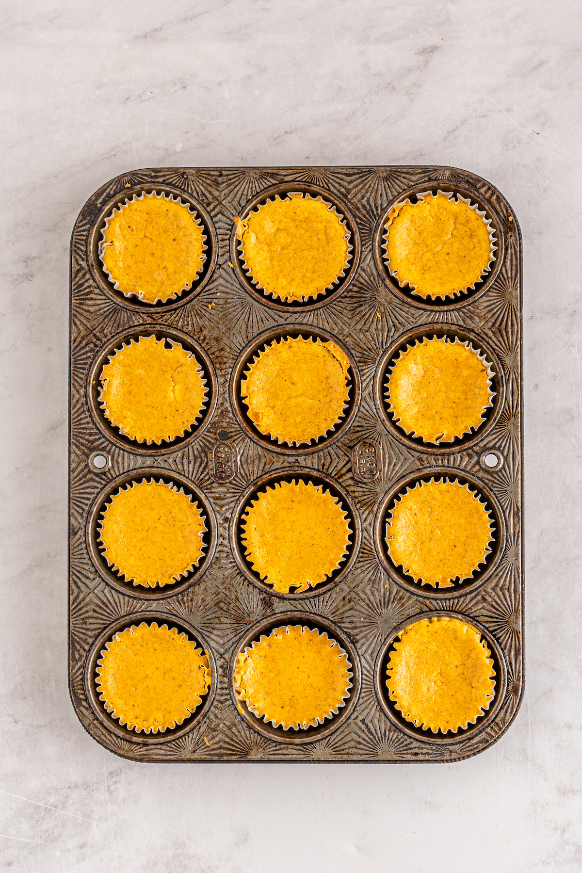 a cupcake tray filled with orange cheesecake filling