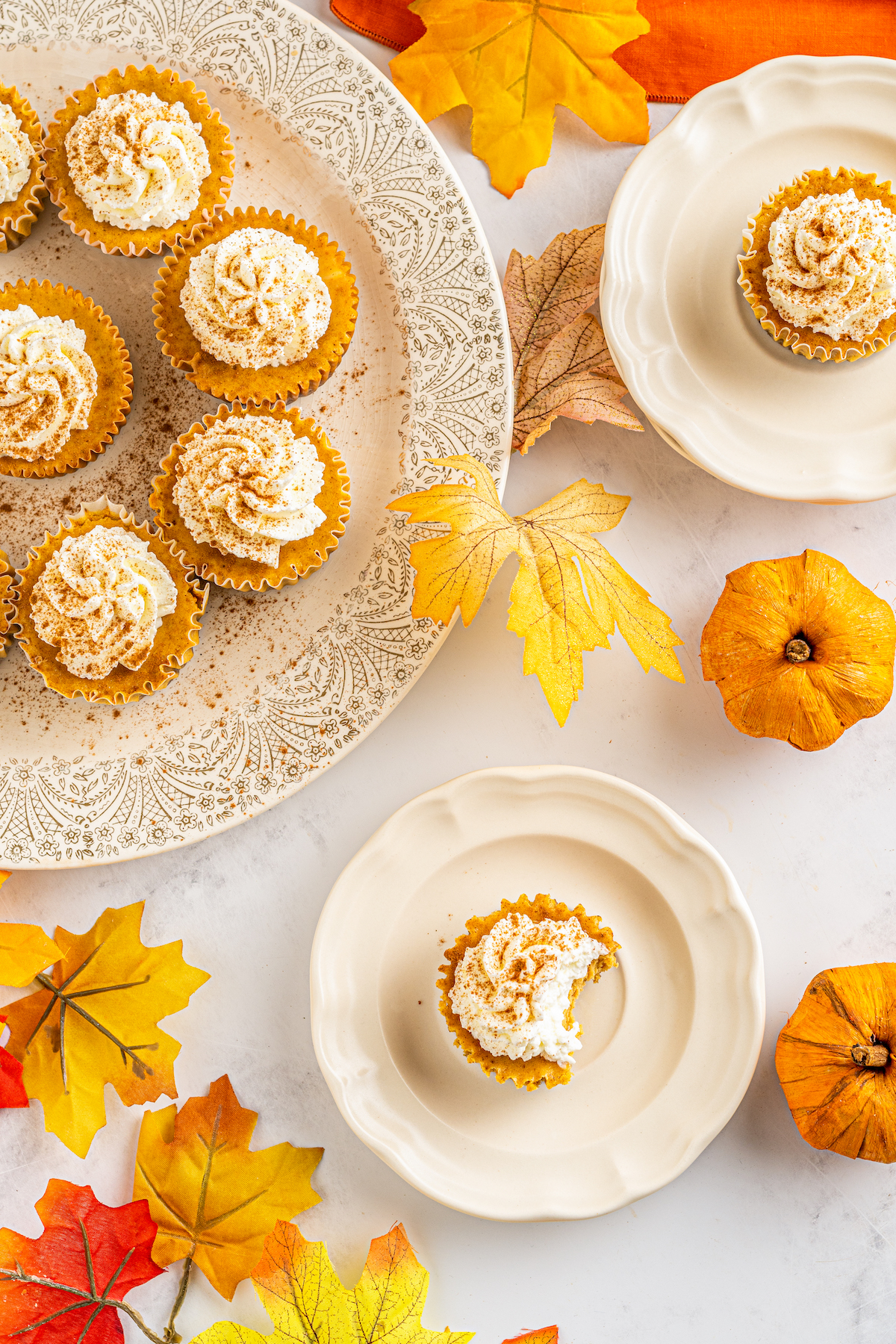 top view of mini cheesecakes with whipped cream on top on a platter and one single mini cheesecake on a small plate with a bite taken out of it