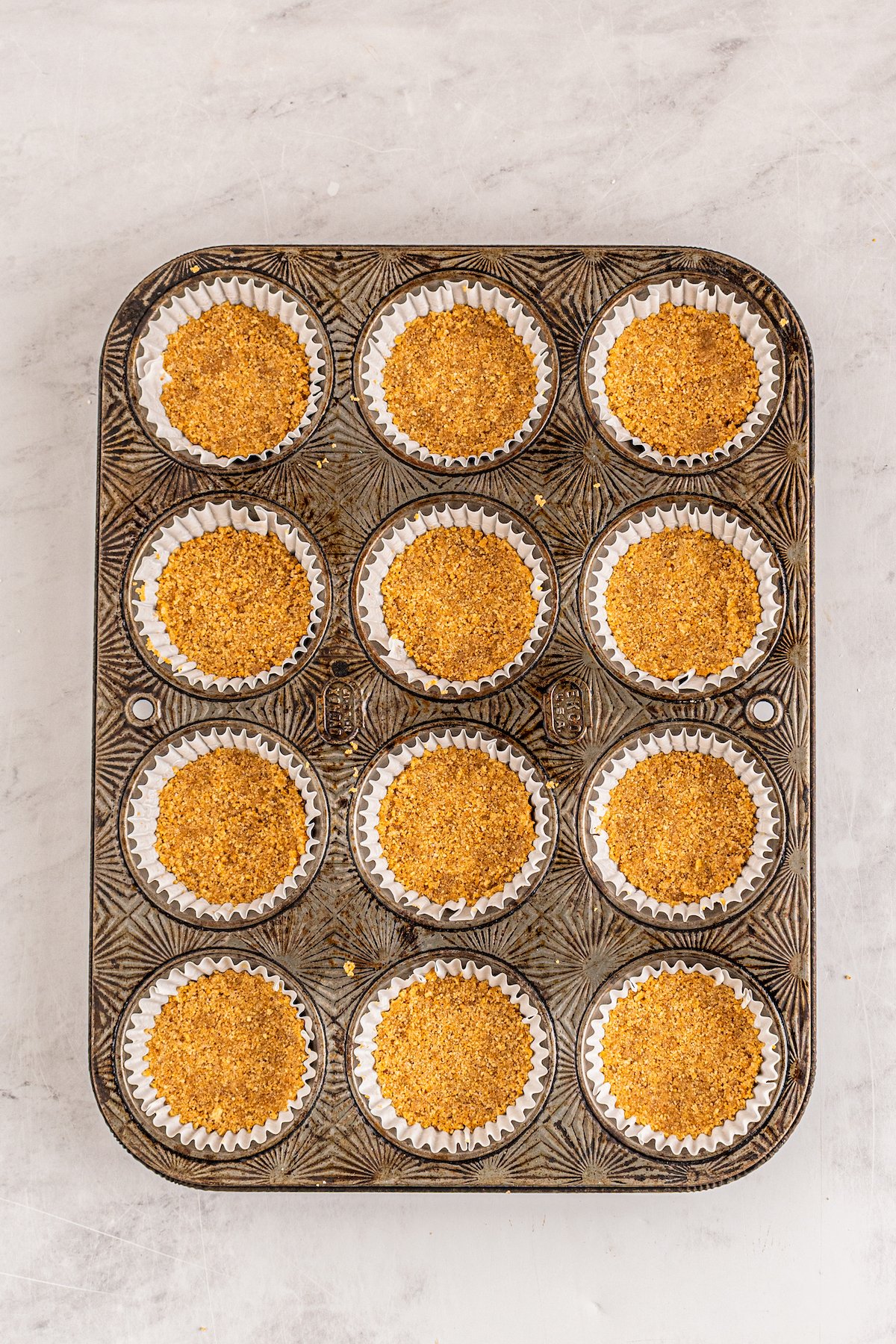 a cupcake tin filled with graham cracker crust in each section