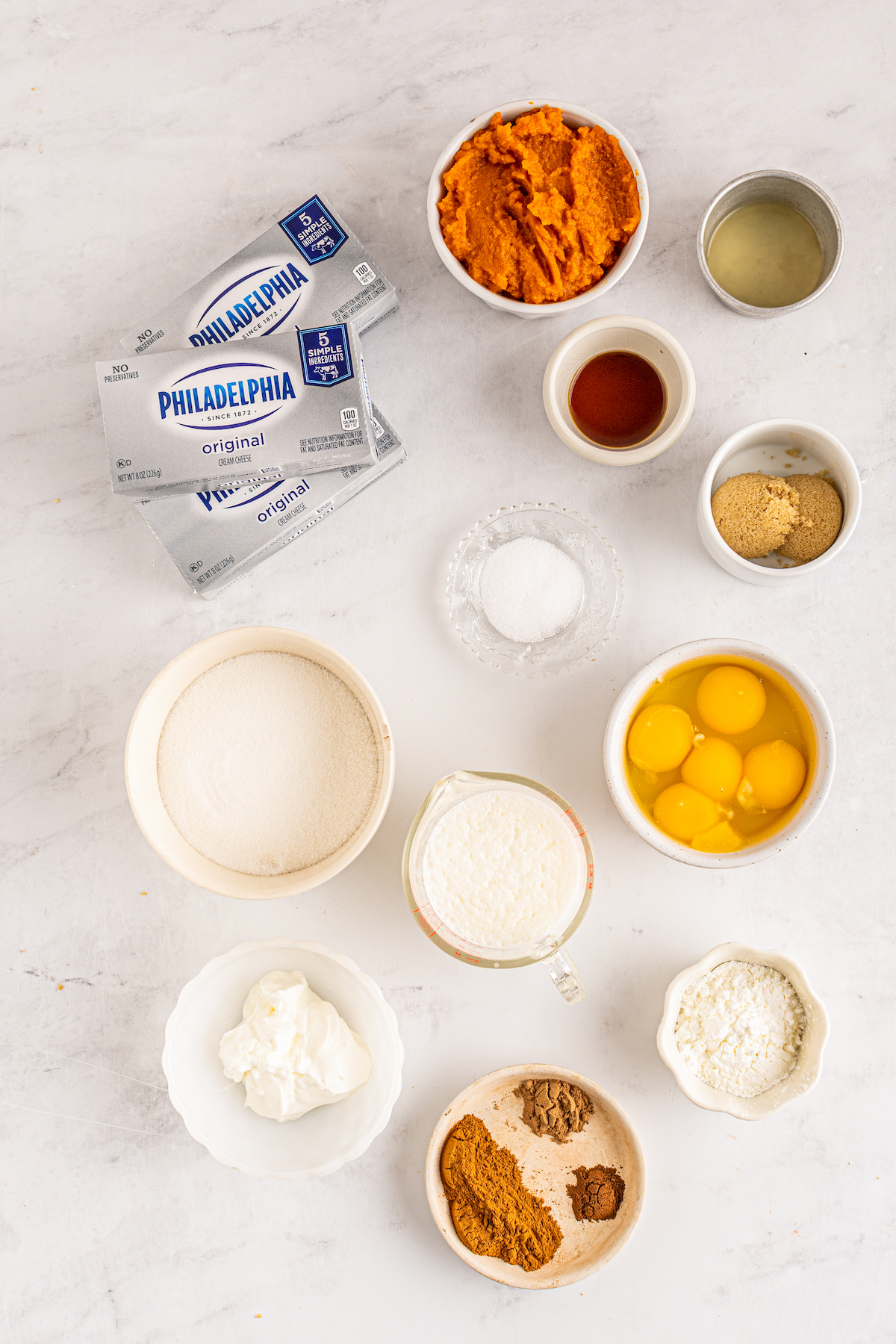 a countertop with cream cheese packages and prep bowls with ingredients to make cheesecake