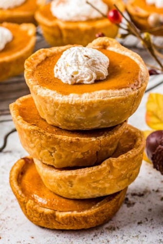 stack of four mini pumpkin pies, the top one has a dollop of whipped cream