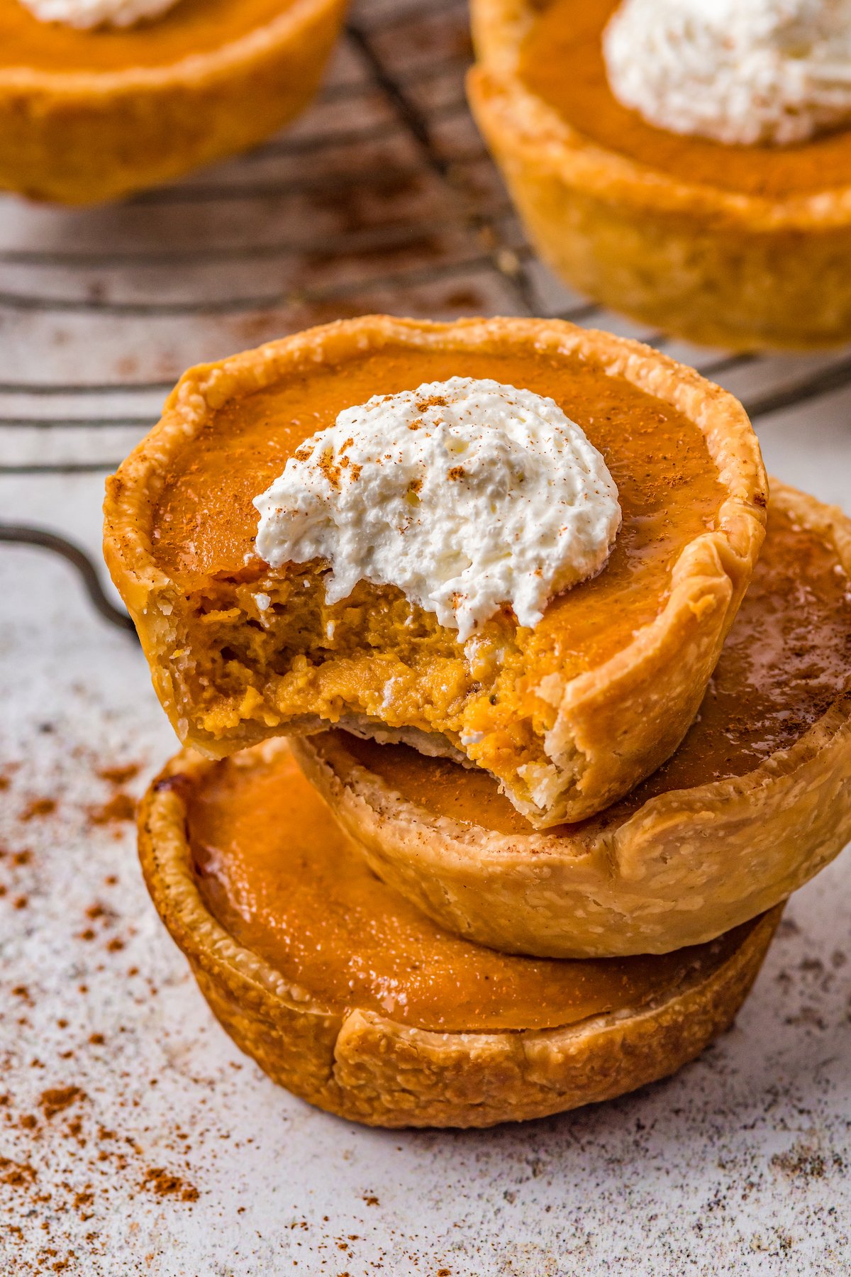 stack of three mini pumpkin pies, the top one has a dollop of whipped cream and a bite taken out of it