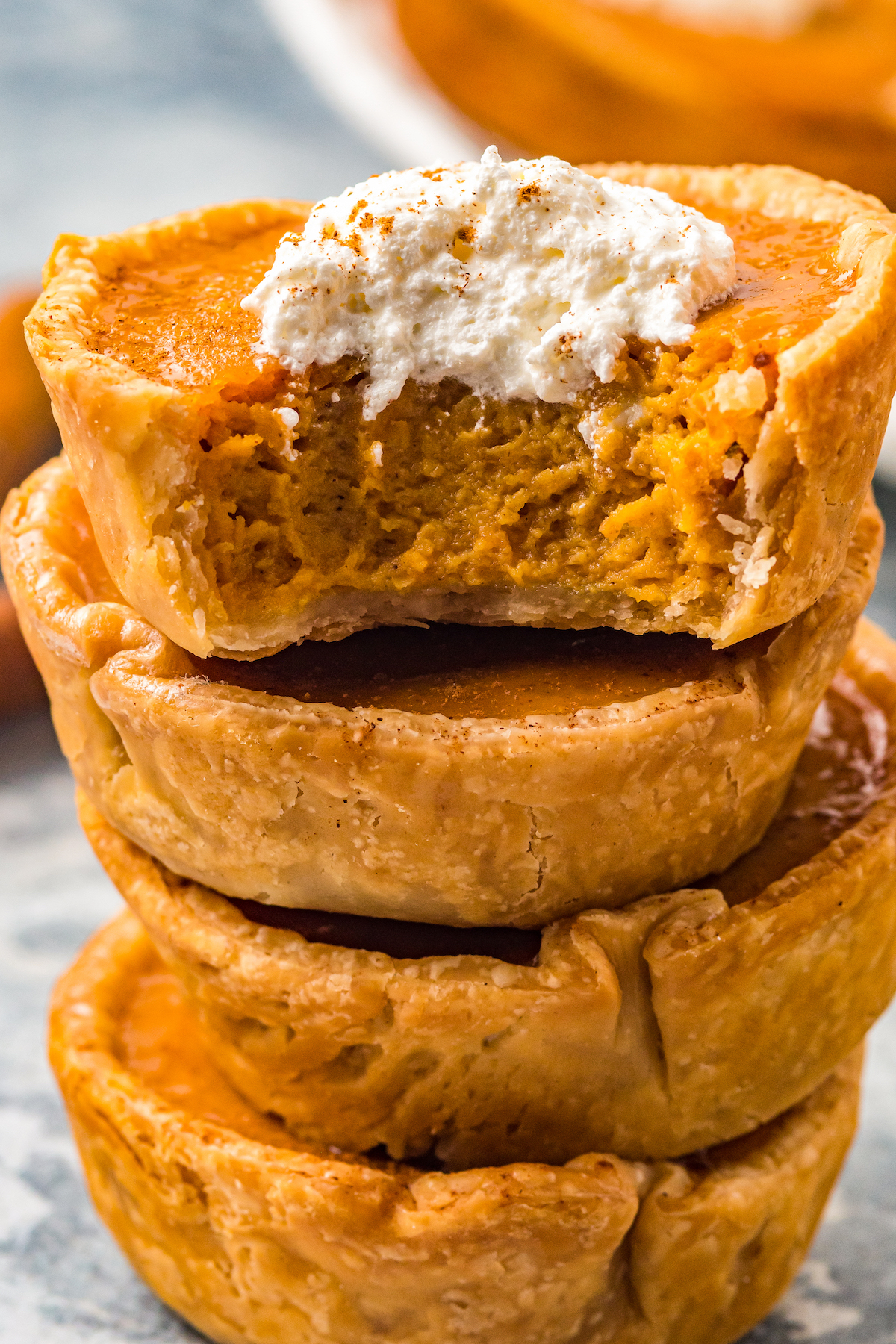 stack of three mini pumpkin pies, the top one has a dollop of whipped cream and a bite taken out of it