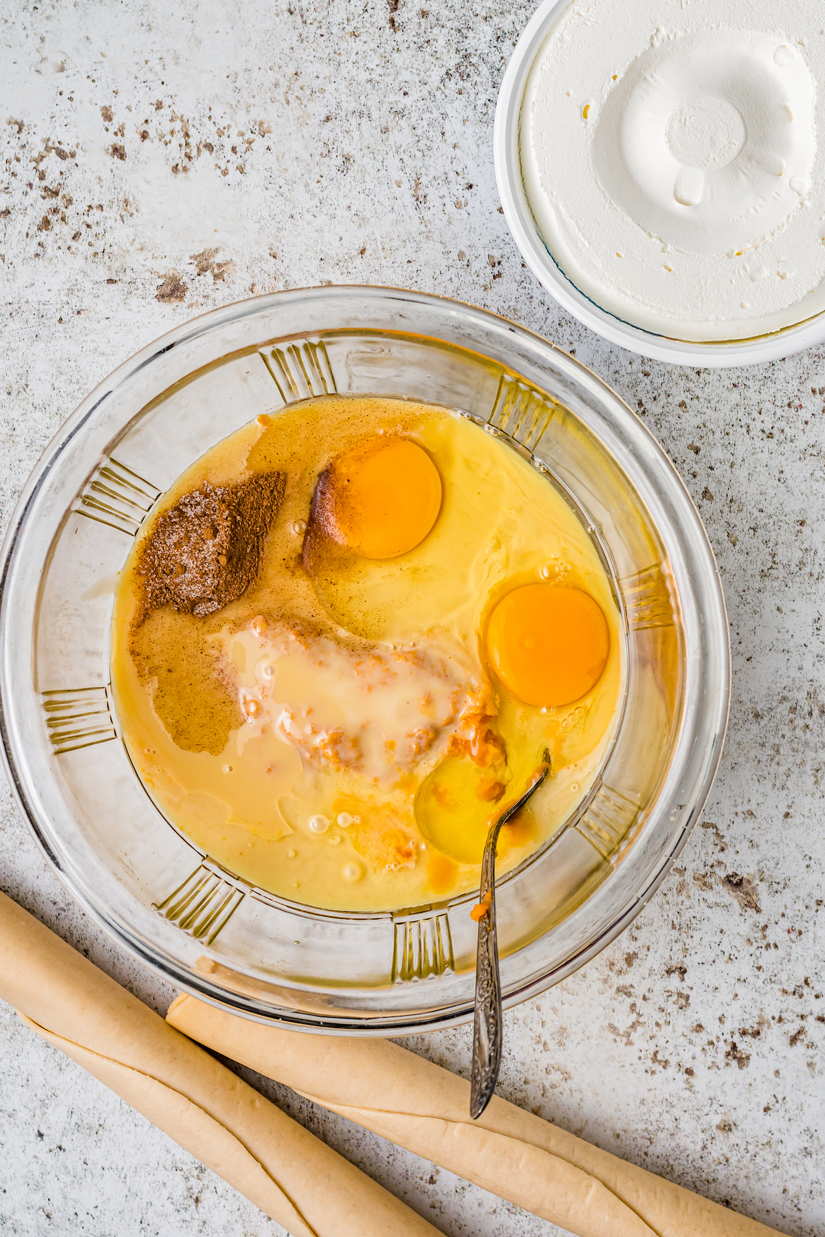 a glass mixing bowl with eggs, pumpkin pie filling, spices, and sugar being mixed