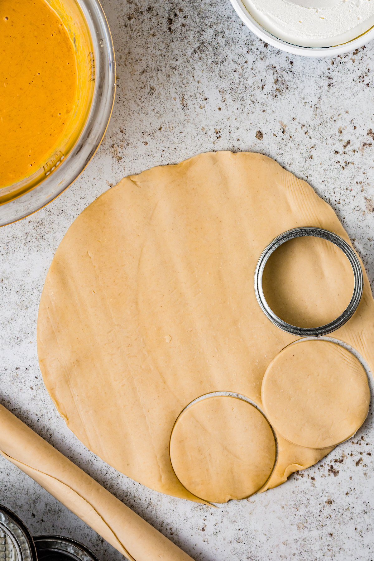 rolled pastry dough with a round cookie cutter cutting out small pie crusts