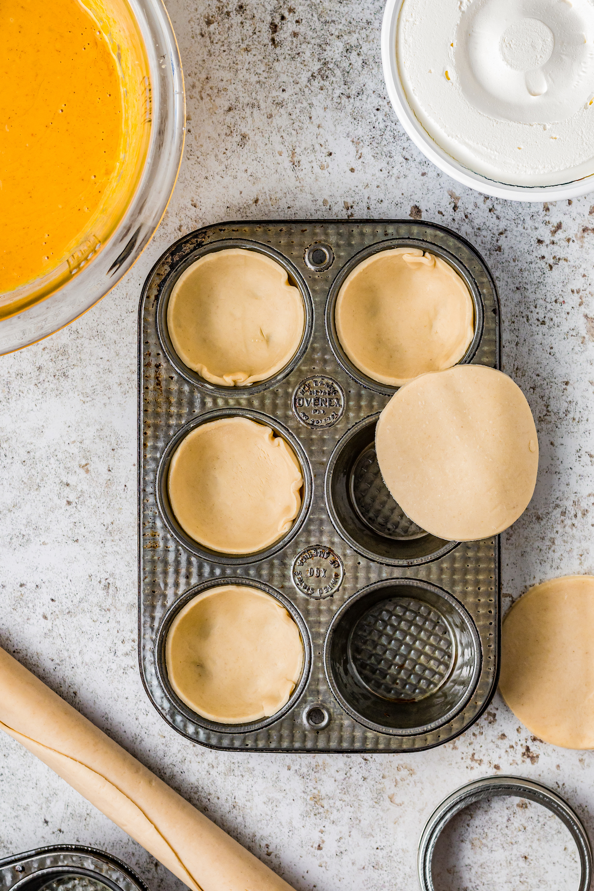 a muffin pan being lined with small rounds of pastry dough