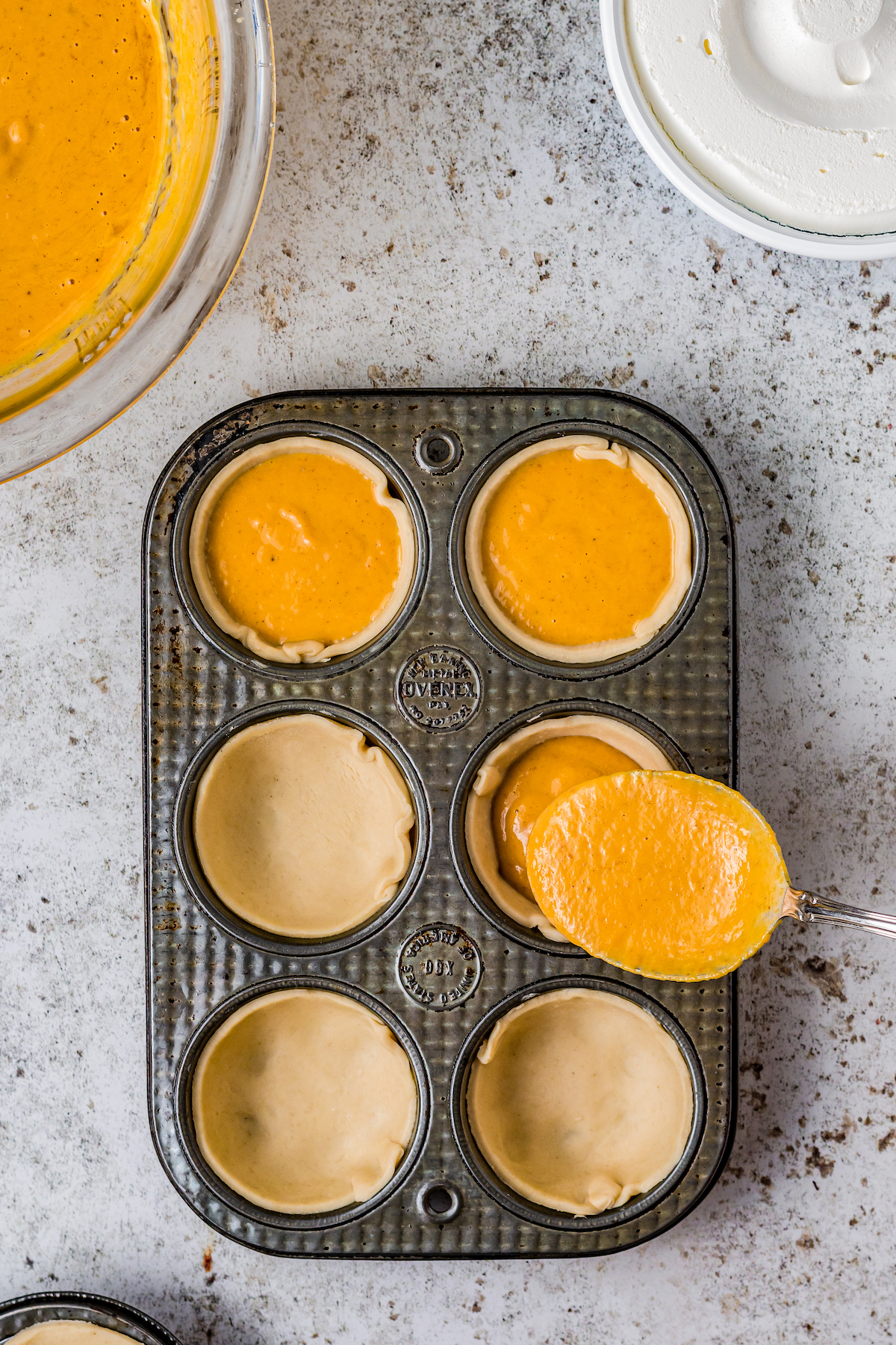 a muffin pan that has pastry dough in each tin and being filled with orange pie filling
