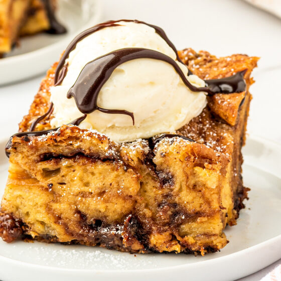 A slice of Nutella Croissant Bread Pudding on a plate with ice cream on top and chocolate sauce.