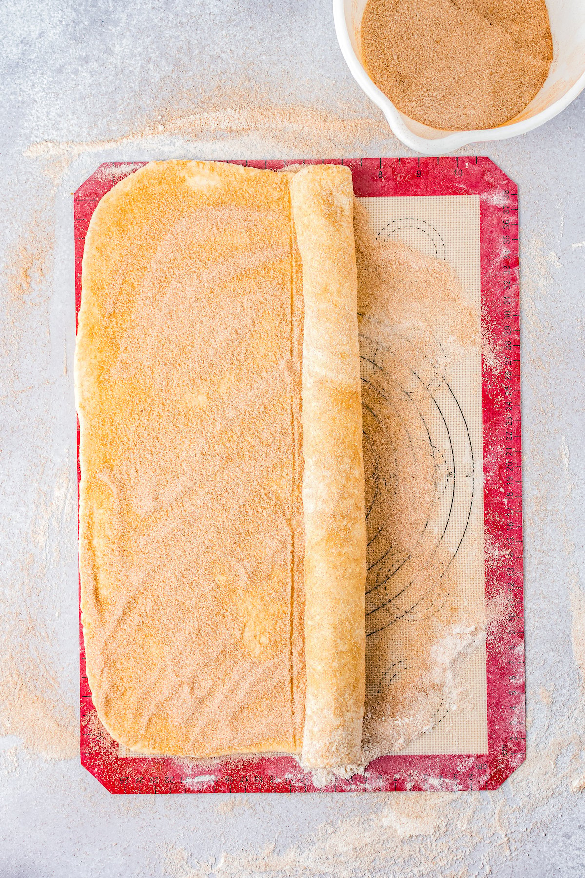 a large sheet of dough covered in cinnamon sugar being rolled up lengthwise