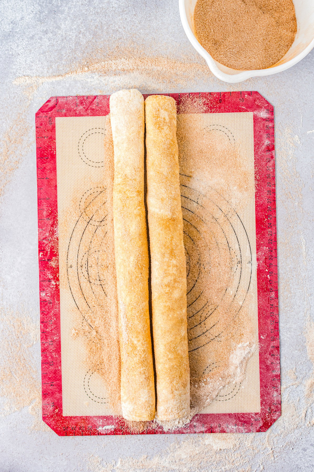 two sections of rolled dough rolled in cinnamon sugar on a silicone mat