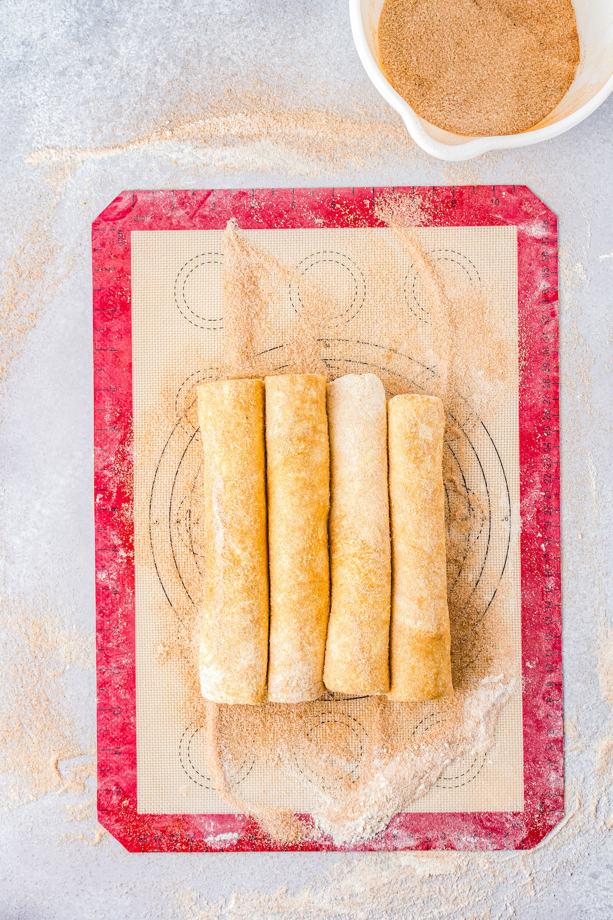 four sections of rolled dough rolled in cinnamon sugar on a silicone mat
