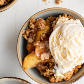 Peach crisp in bowls with ice cream on top of one serving.