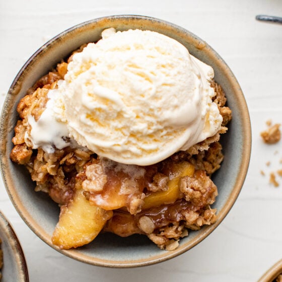 Three bowls of peach crisp with vanilla ice cream on top of one of the servings.