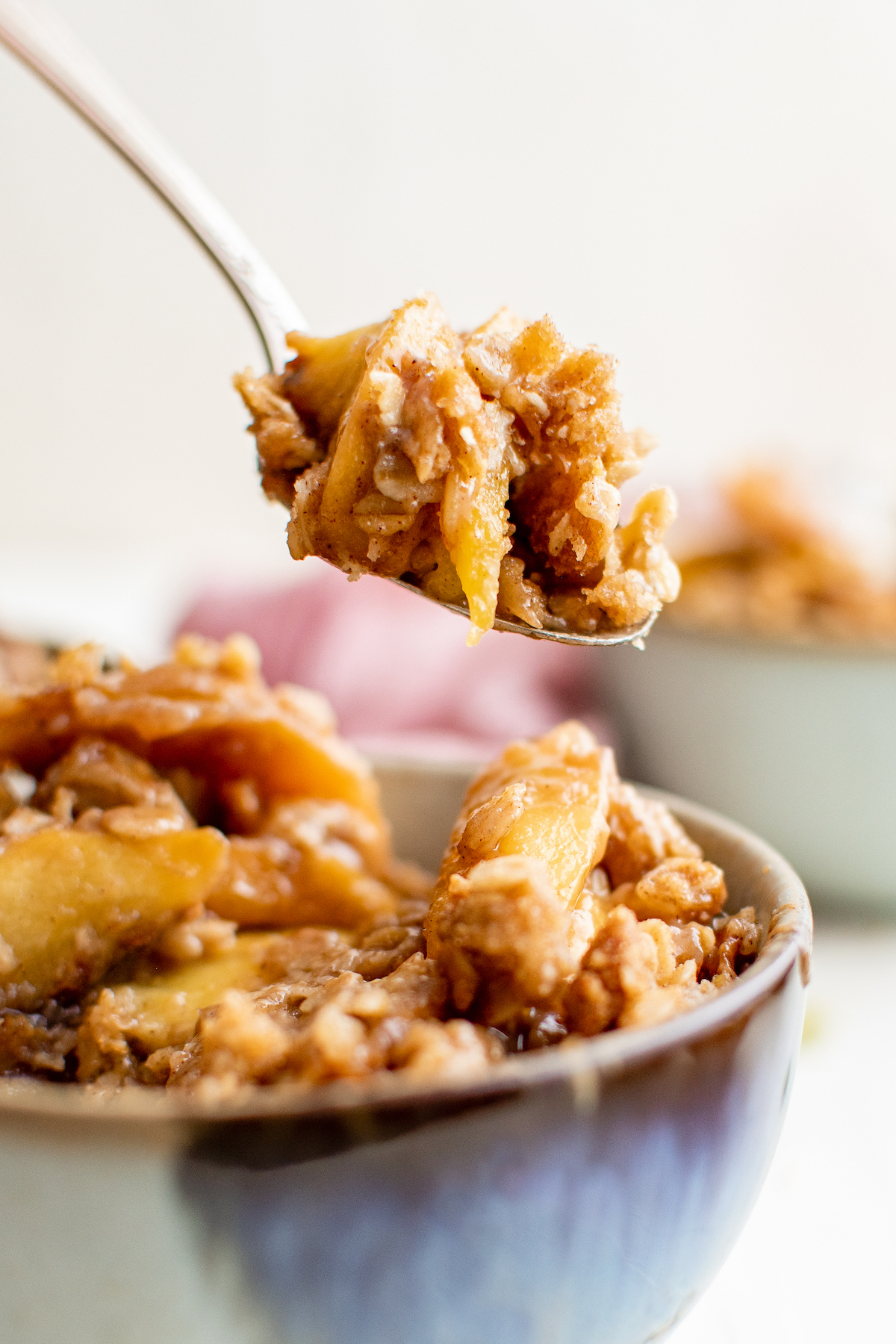 A spoonful of peach crisp being scooped up from a bowl.