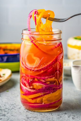 a jar of pickled red onions and peppers with a fork removing some of the pickled vegetables