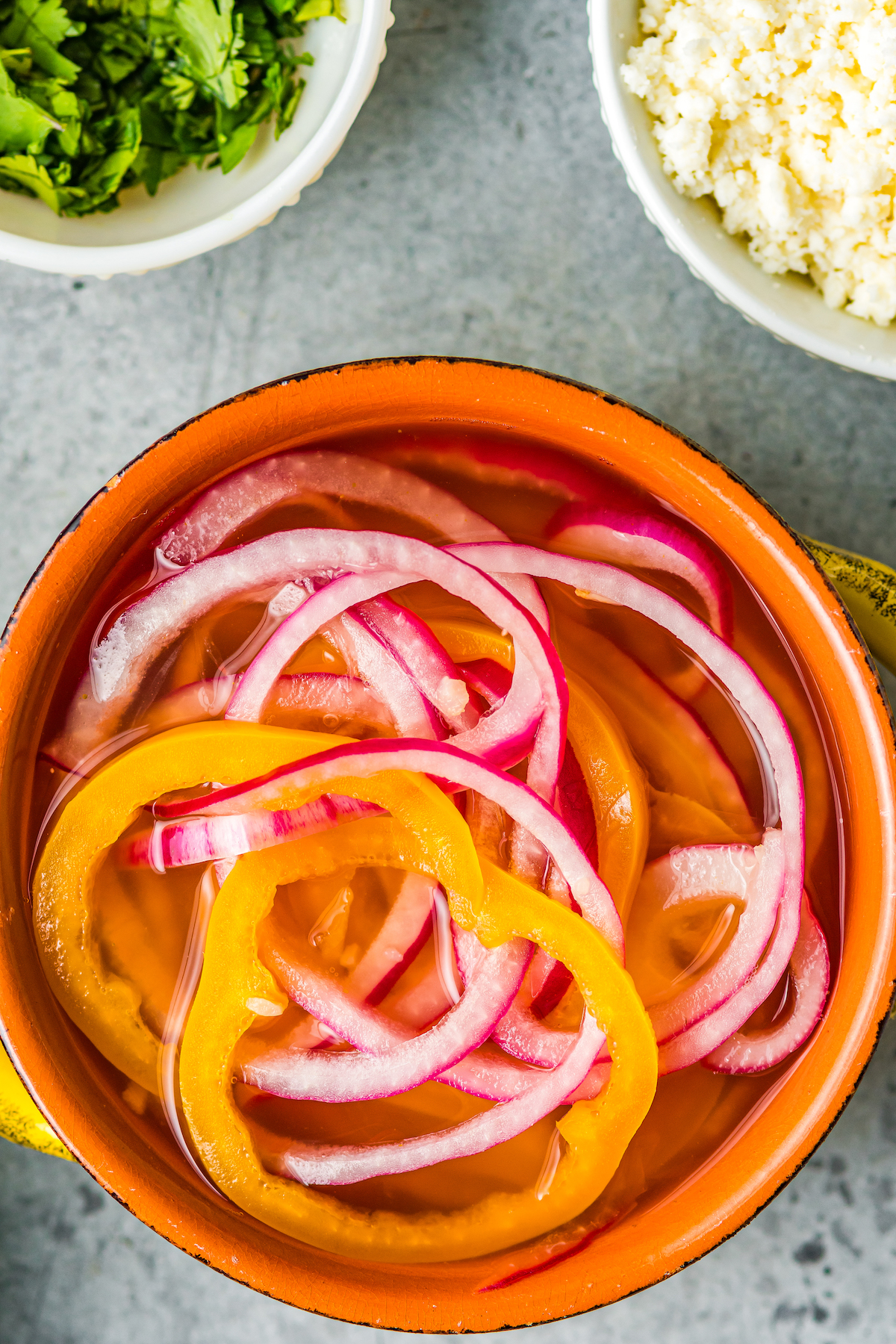 sliced red onions and habaneros in pickling brine in a small crock