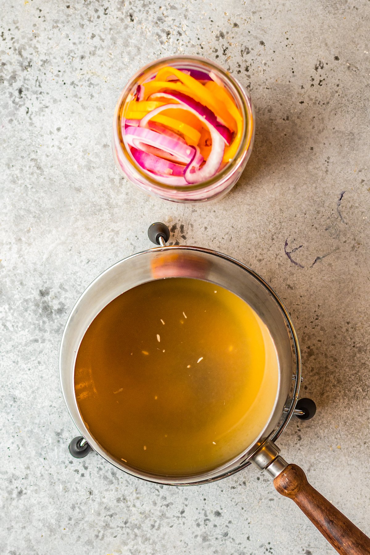 pickling brine in a pot next to onions and peppers in a mason jar