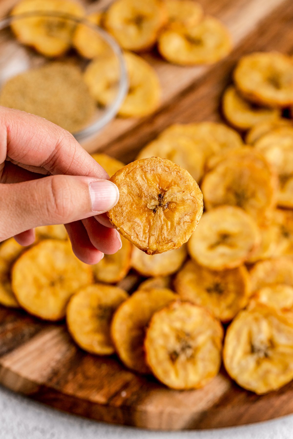 Baked plantain rounds, with one held up to the camera to show the size.