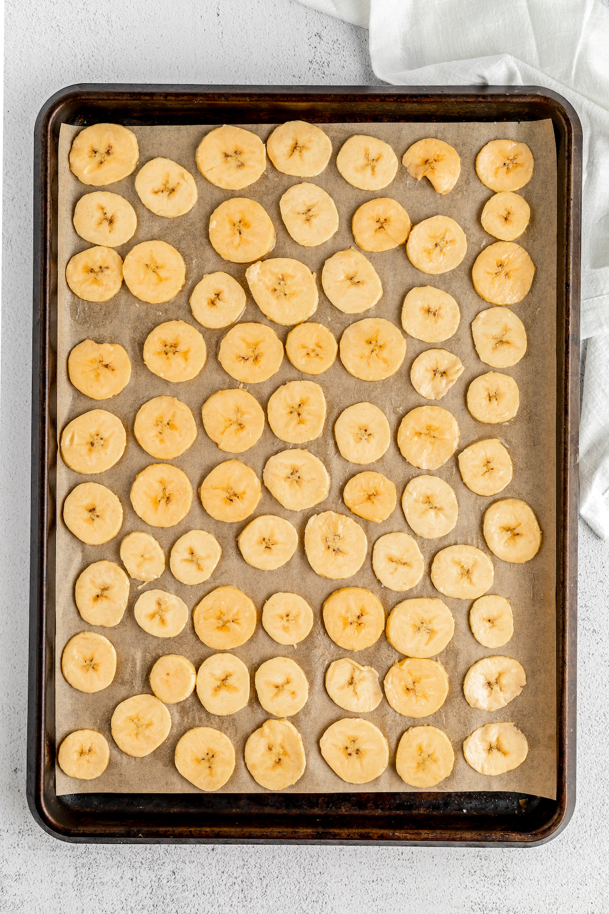 Overhead shot of raw plantain slices on a baking sheet.