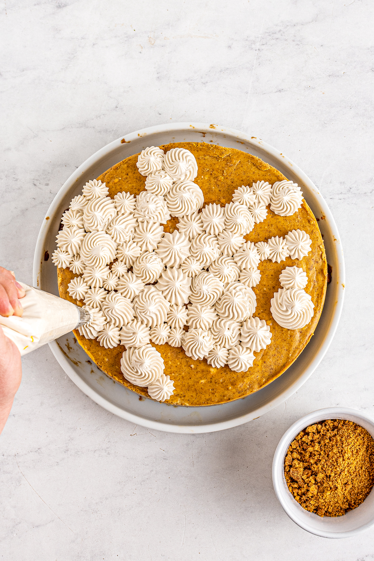 Frosting being piped onto a baked pumpkin cheesecake.