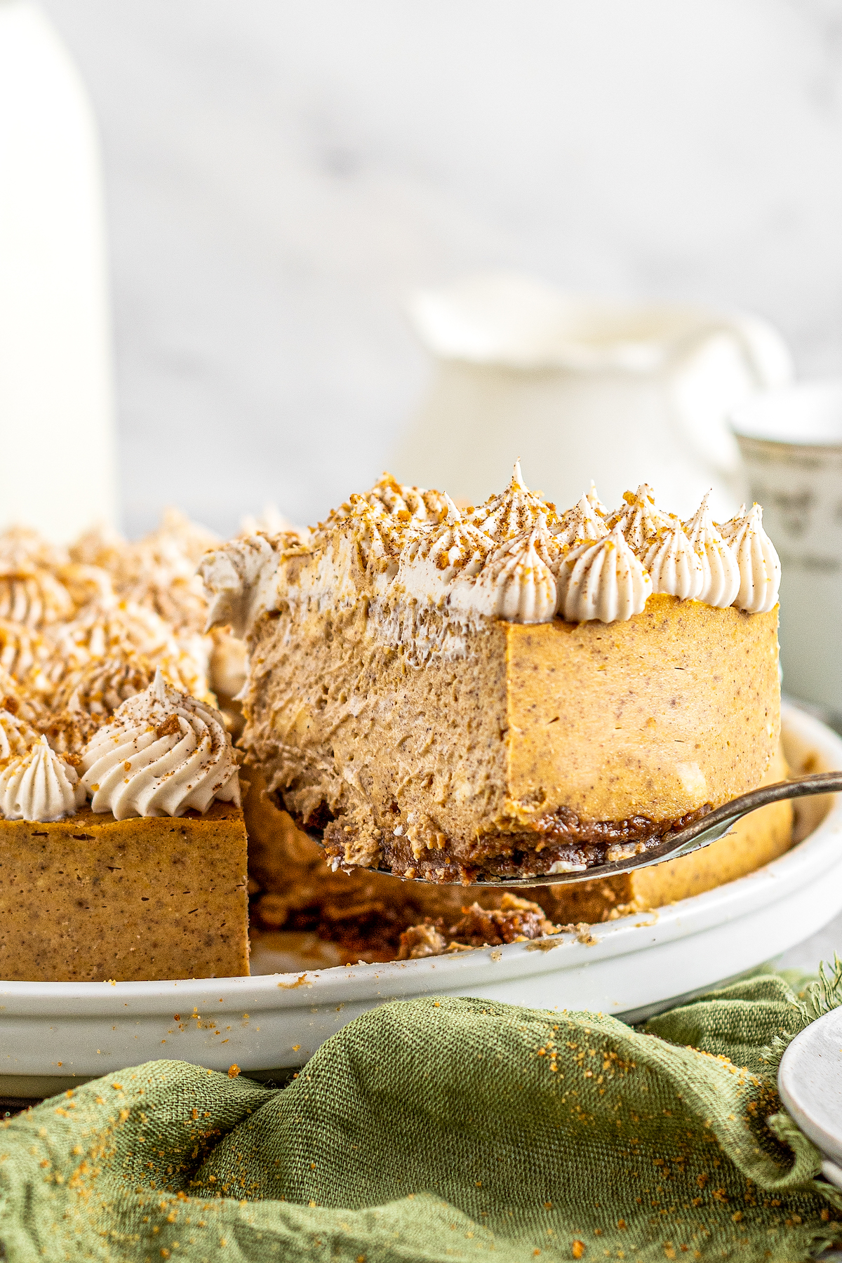 A slice of pumpkin cheesecake with gingersnap crust being lifted from a cake plate.
