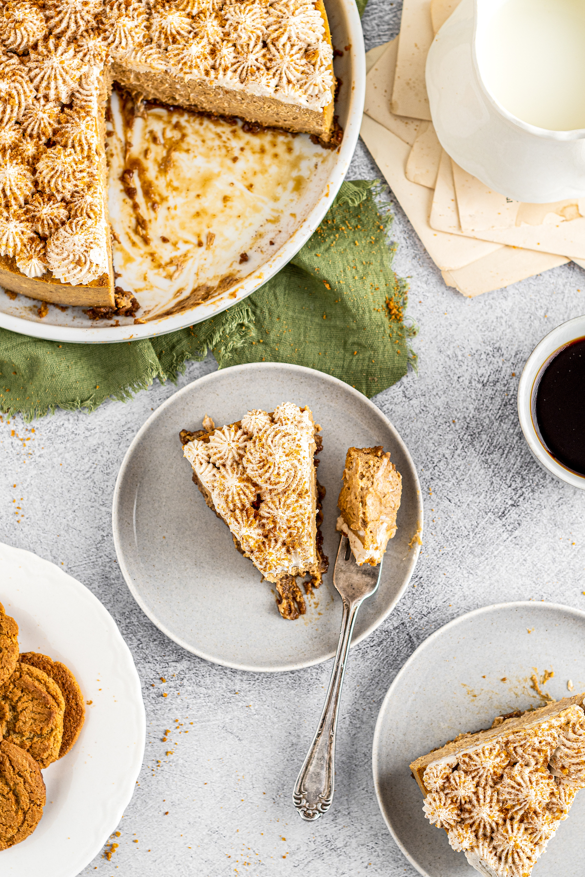 Overhead shot of a table with a large cheesecake, slices of cheesecake on plates, coffee, and more.