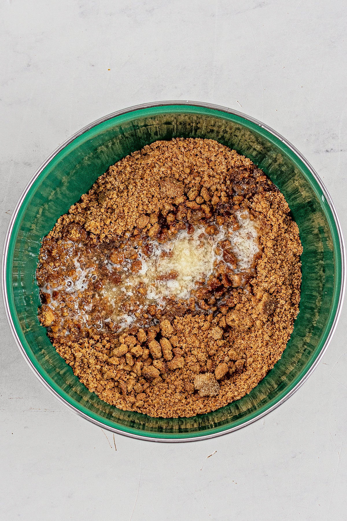 Crushed cookies, butter, and brown sugar in a green mixing bowl.