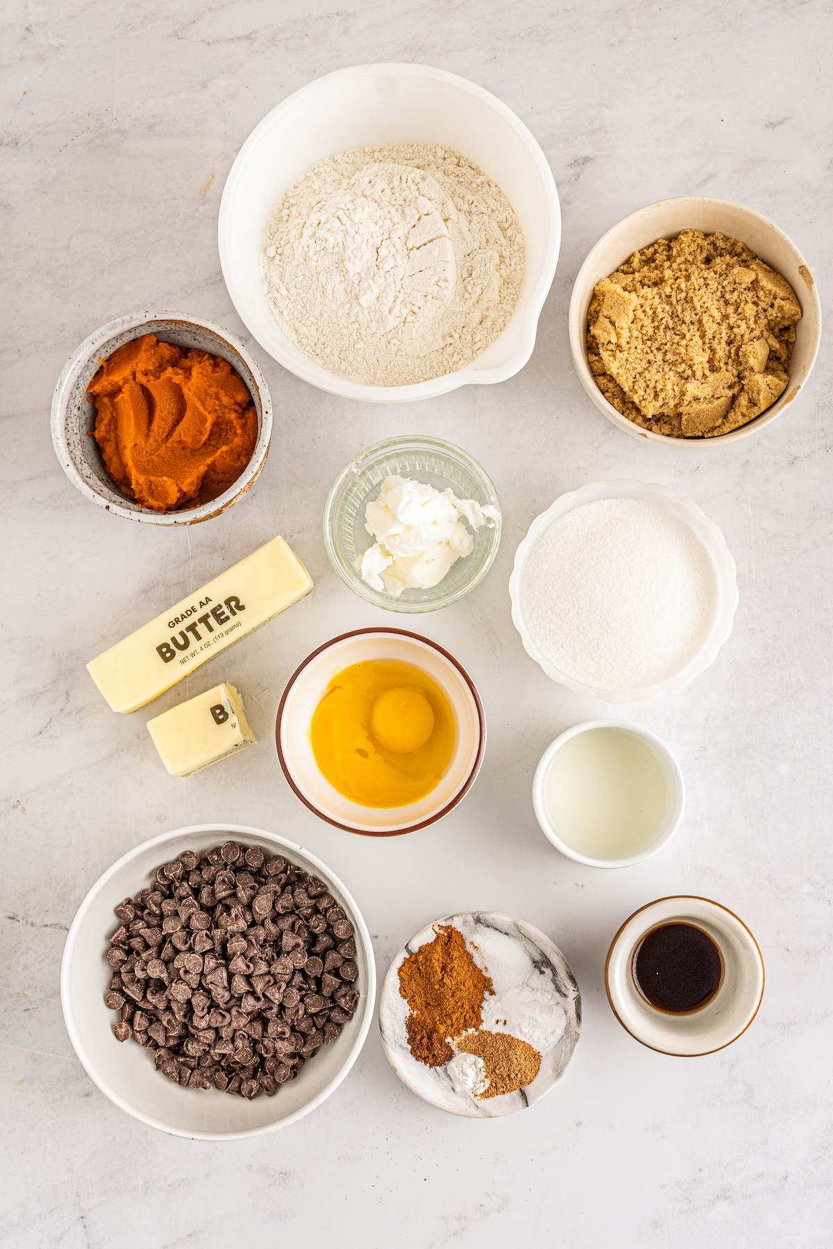 the ingredients needed to make pumpkin chocolate chip cookies like butter, pureed pumpkin, flour, brown sugar, white sugar, eggs, spices, vanilla, and chocolate chips prepped and ready to be mixed