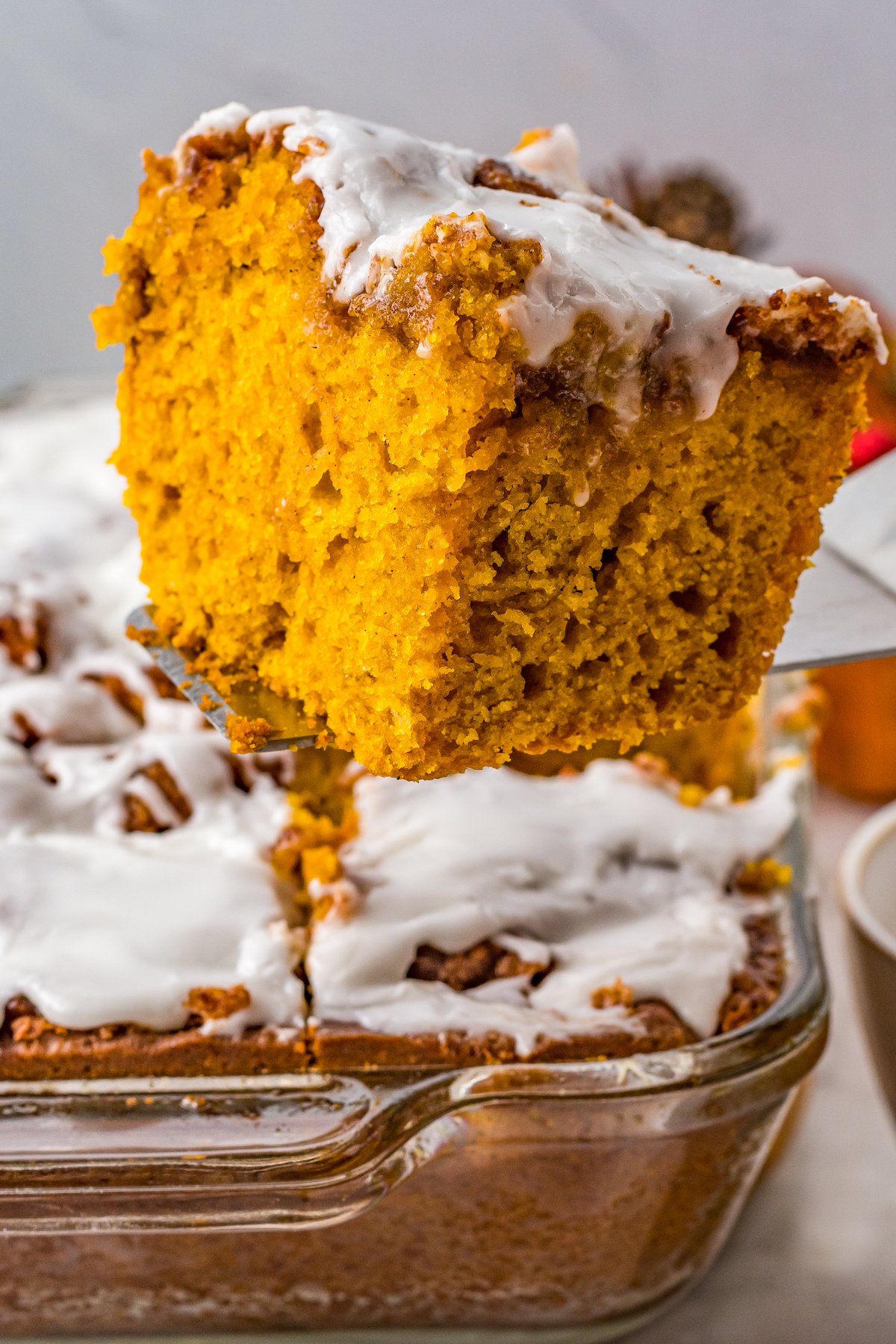 A serving of pumpkin cinnamon roll cake being lifted from a glass baking dish.
