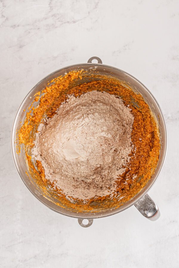 Flour, pumpkin spice, baking powder and baking soda being added to pumpkin cookie dough.