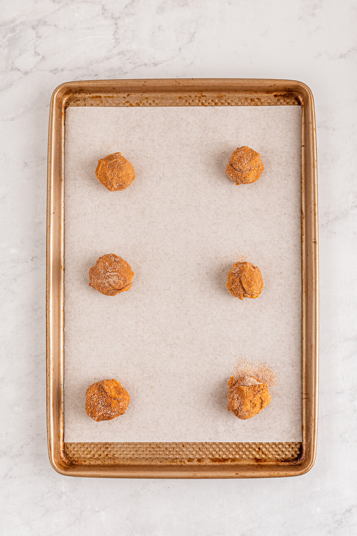 Balls of dough coated in cinnamon sugar on a parchment lined baking sheet.