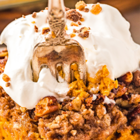A fork taking a bite of pumpkin cake with whipped cream on top.