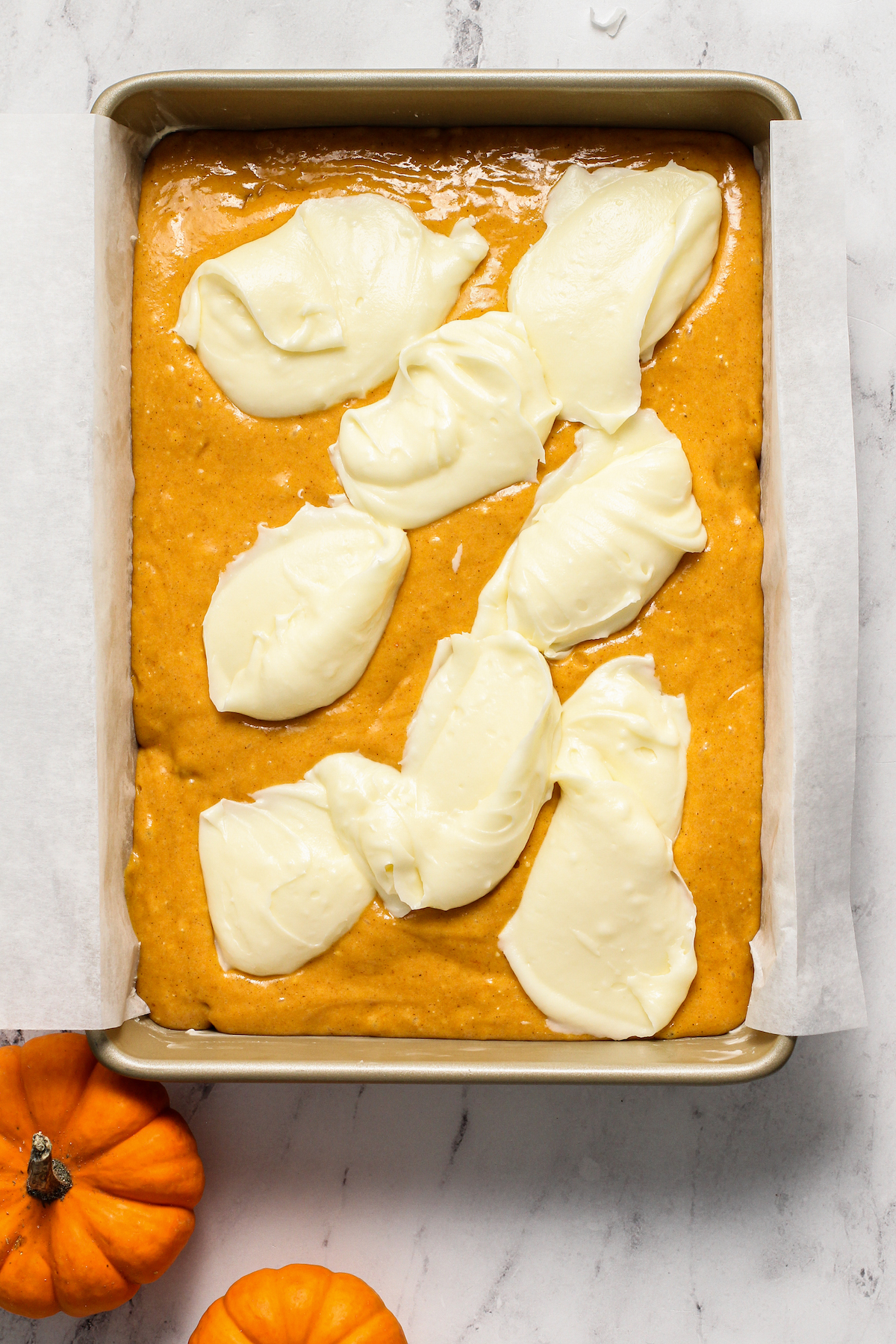 Pumpkin cake batter with thick dollops of cream cheese filling on top.
