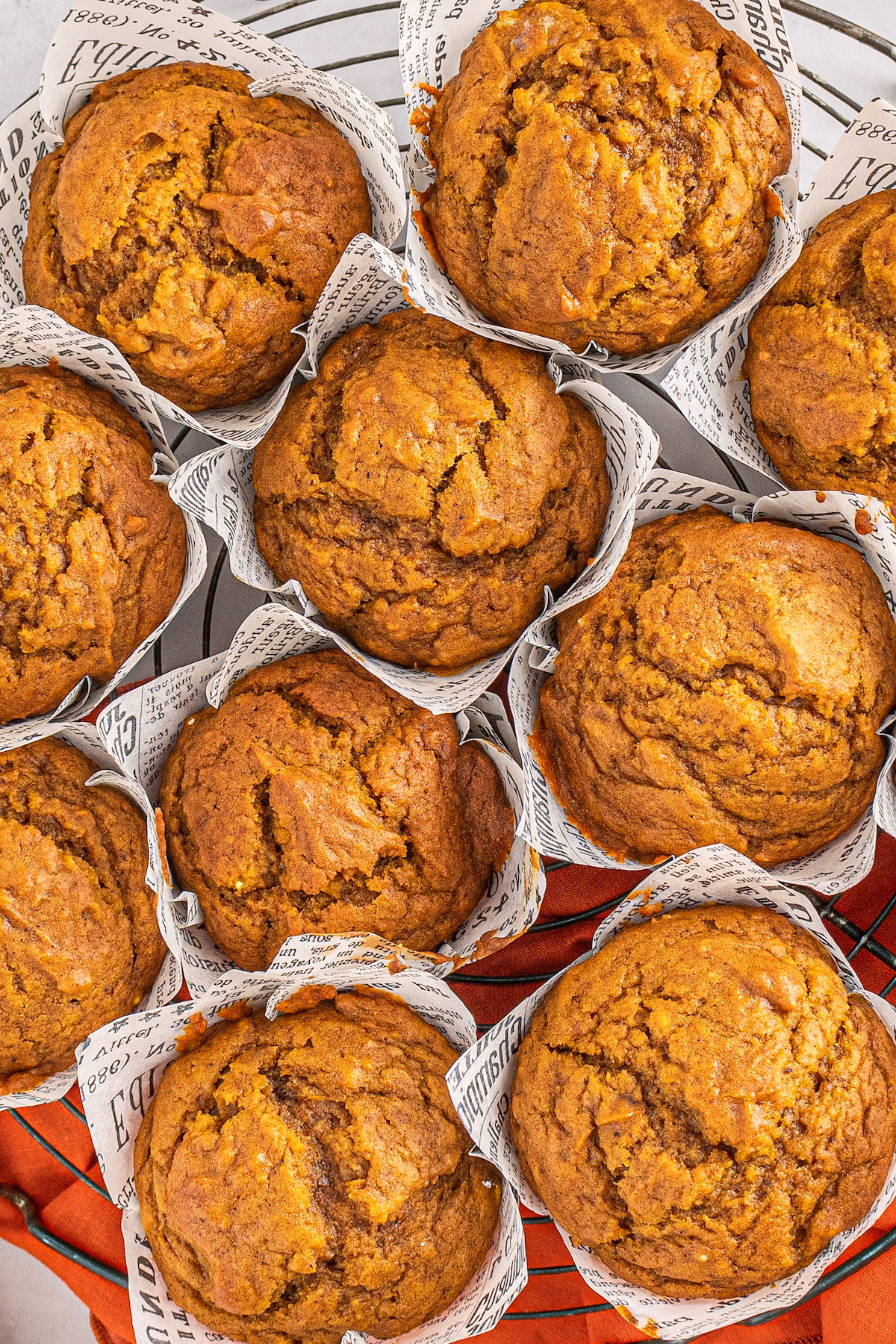Large pumpkin muffins with liners on a cooling rack.