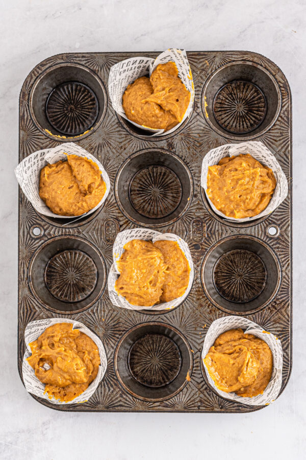 A muffin tin with every other well filled with liners and muffin batter.