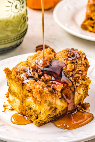 A single serving of Pumpkin Pecan French Toast Casserole with maple syrup being poured over the top of it.