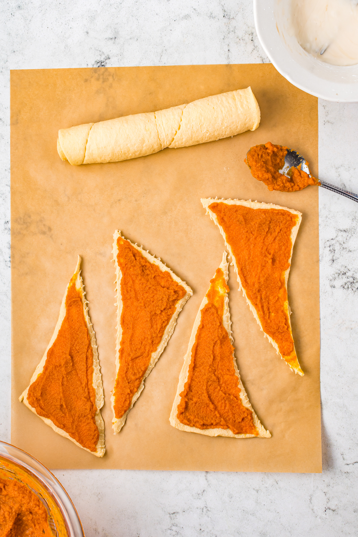 Pumpkin pie filling being spread over triangles of crescent dough.